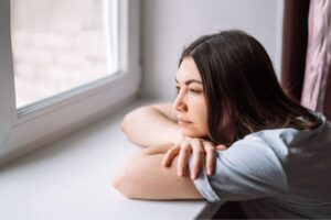 Frau sieht schweigend aus dem Fenster – Sprachlosigkeit als Traumafolge